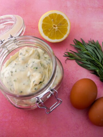 A jar of tarragon mayonnaise set aside 2 brown eggs, a lemon and stalks of fresh tarragon.