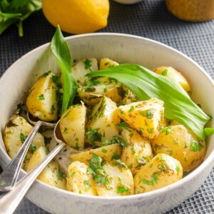 A bowl of warm wild garlic potato salad in a lemon and mustard dressing garnished with wild garlic and freshly chopped parsley.