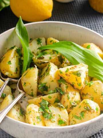 A bowl of warm wild garlic potato salad in a lemon and mustard dressing garnished with wild garlic and freshly chopped parsley.