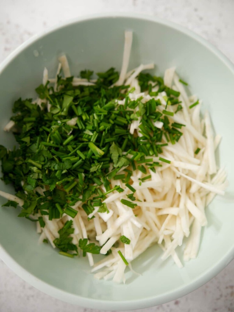 A bowl of salad dressing with added celeriac and freshly chopped chives and parsley.