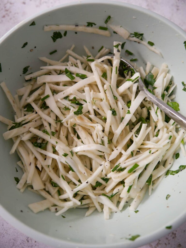 A bowl of celeriac remoulade coated in dressing with added fresh herbs.
