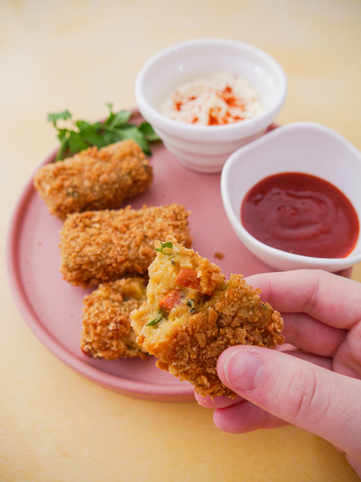 A plate with 3 Spanish chorizo chicken croquettes and bowls of mayonnaise and chilli sauce set alongside. Also a hand holding half a croquette.