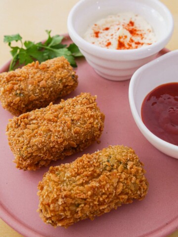 A plate with 3 Spanish chorizo chicken croquettes and bowls of mayonnaise and chilli sauce set alongside.