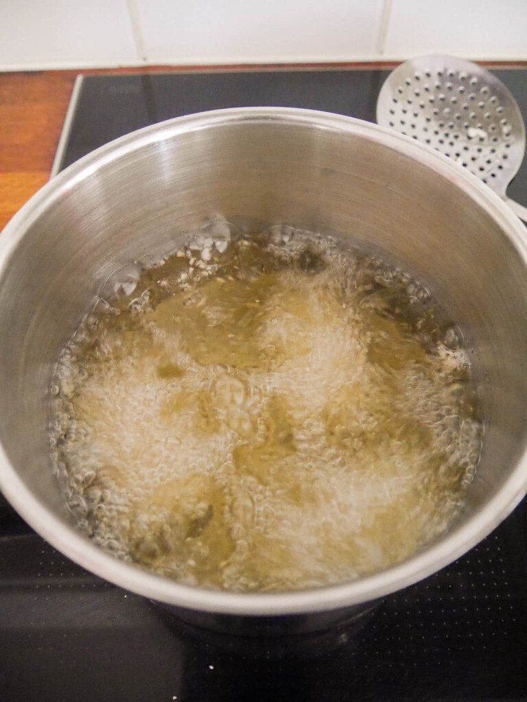 A large saucepan filled with oil and 3 croquettes cooking in the hot oil.