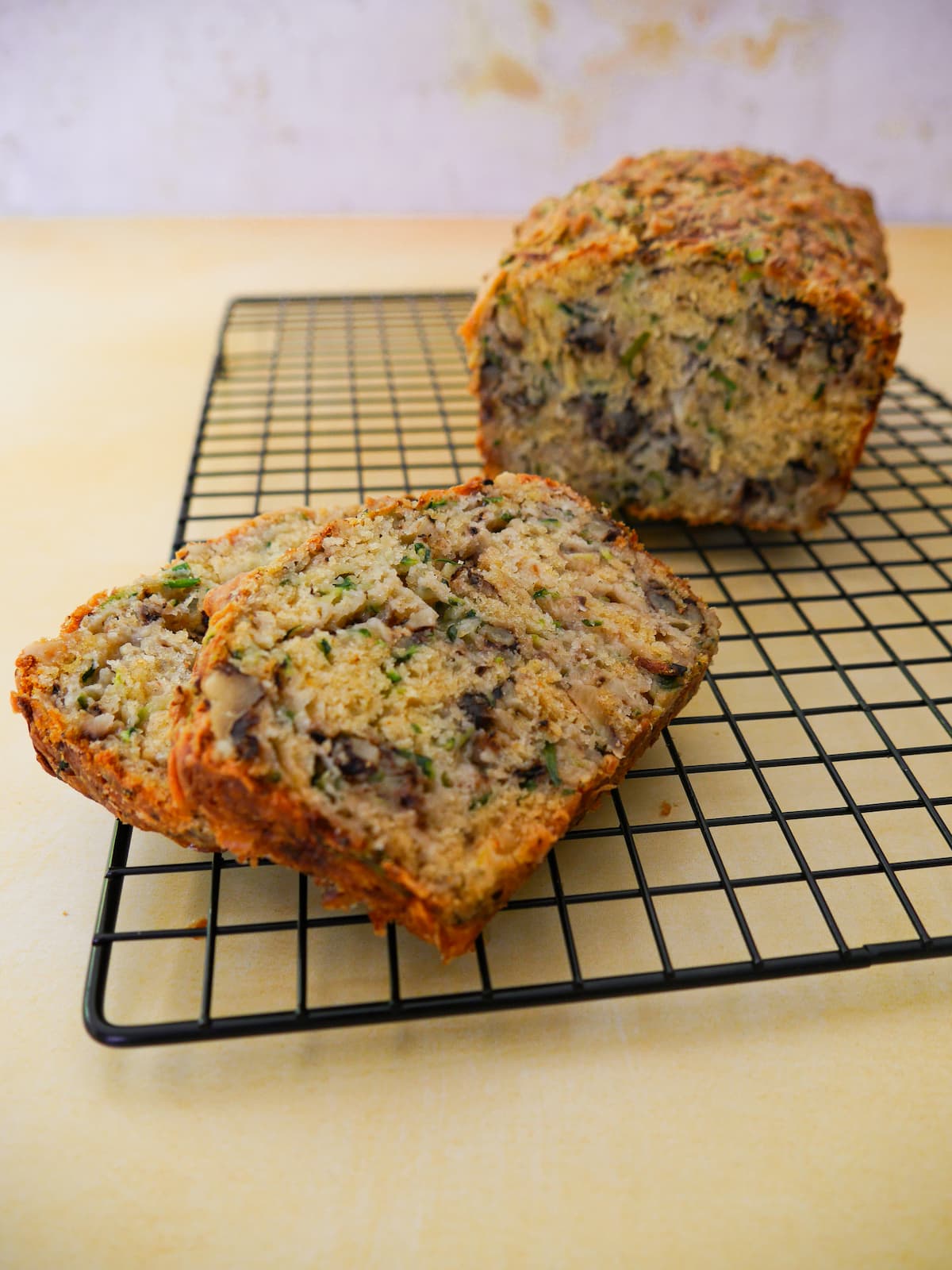 Courgette and cheese bread with walnuts on a wire cooling rack with two slices cut from it.