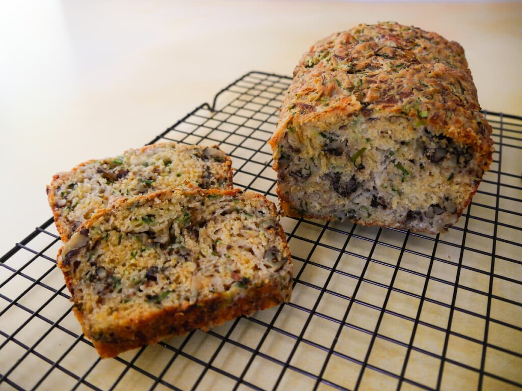 Courgette and cheese bread with walnuts on a wire cooling rack with two slices cut from it.