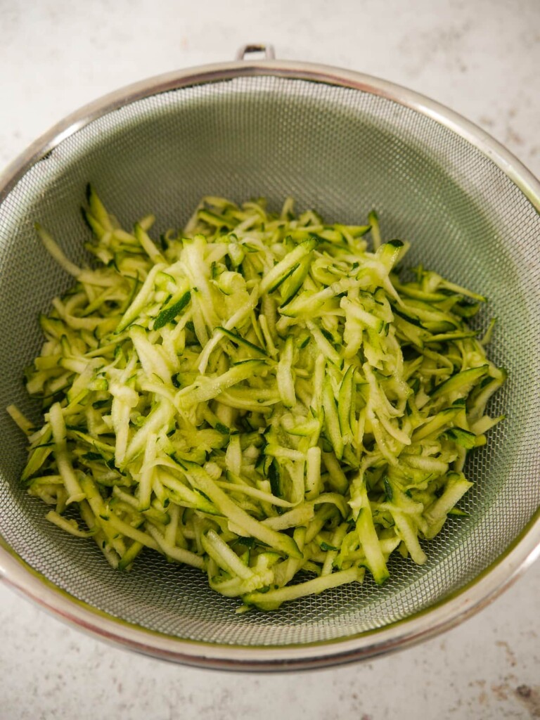 Roughly grated and salted courgette (zucchini) placed in a wire sieve over a bowl, to allow excess water to drain off.