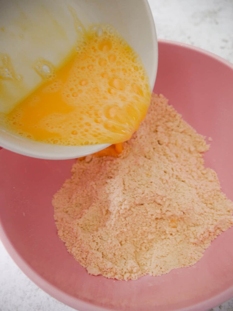 Beaten eggs and milk being added to a bowl of flour and butter breadcrumb mixture.
