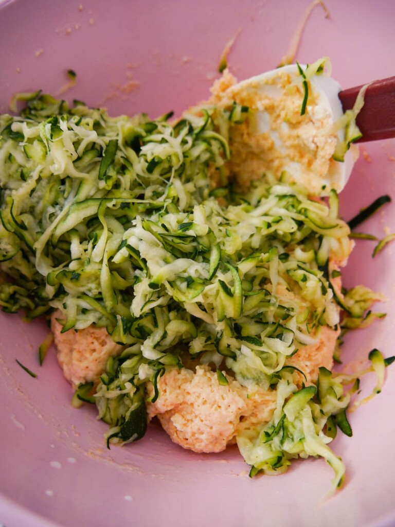 Grated courgette being added to a ball of bread dough.