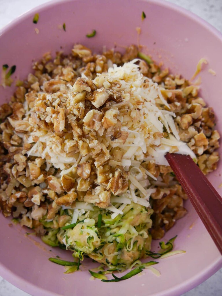 Grated cheese and chopped walnuts being added to a ball of courgette bread dough.