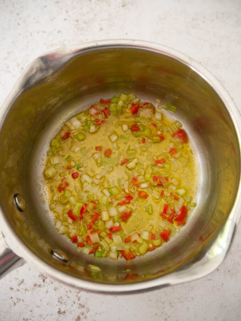 A small saucepan of melted butter with sauteed spring onion, garlic and red chilli.