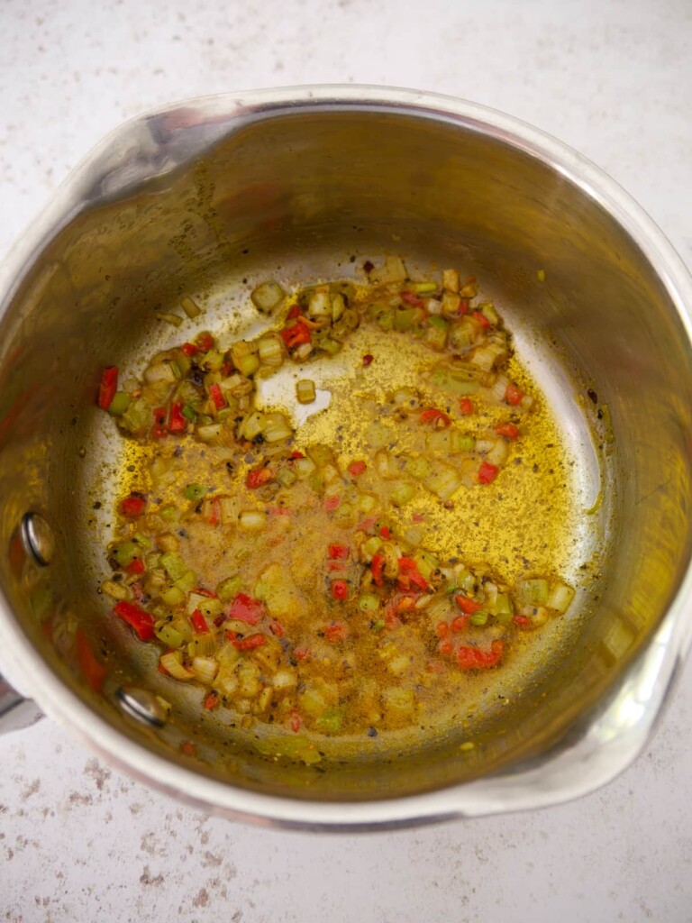 A saucepan with sauteed spring onion, garlic and red chilli with added curry powder, black pepper and sea salt.
