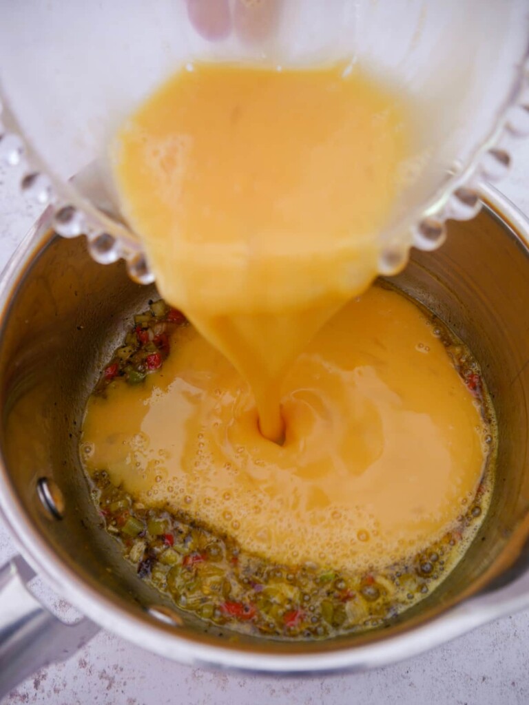 Beaten eggs being poured into a saucepan of curried spring onion, garlic and chilli.