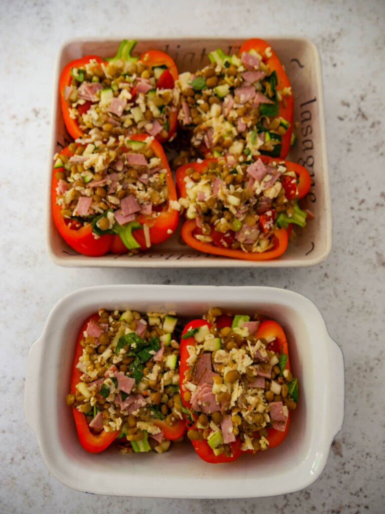 Two oven safe dishes filled with 6 halves of stuffed red bell peppers.