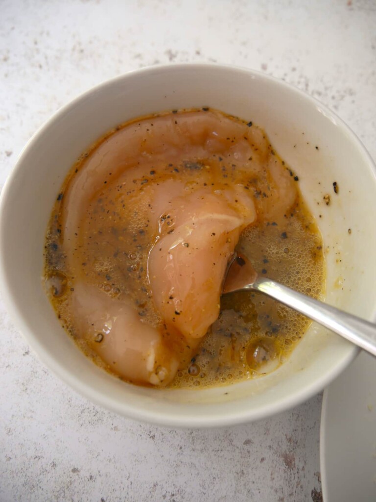 Chicken breast being coated in layer of seasoned beaten egg.