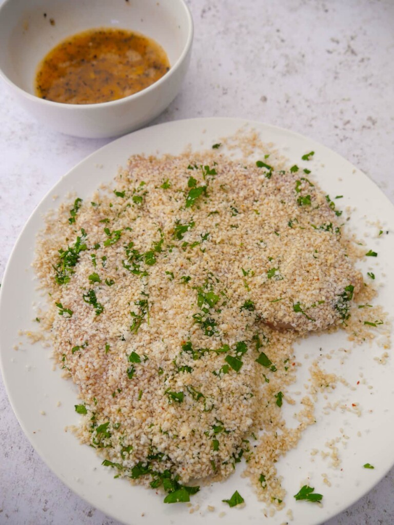 Two chicken breasts coated in a crumb of sesame seeds, grated parmesan cheese and fresh herbs.