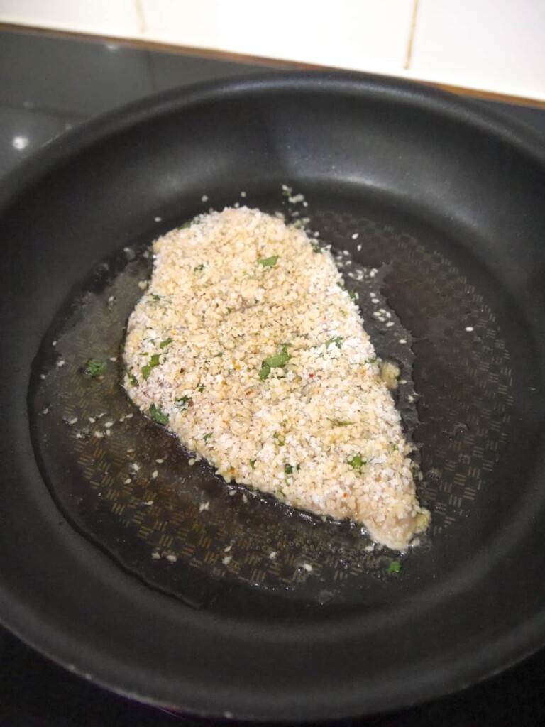 A sesame coated chicken breast being cooked in a non-stick frying pan.