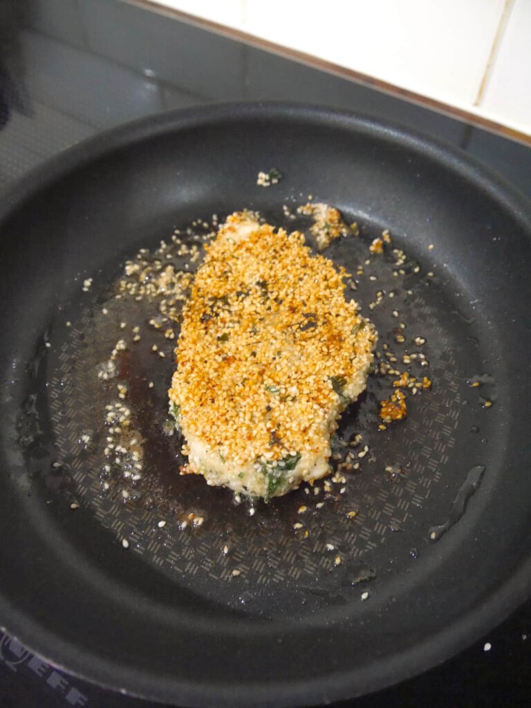 A frying pan with a cooked, golden sesame crusted chicken breast.