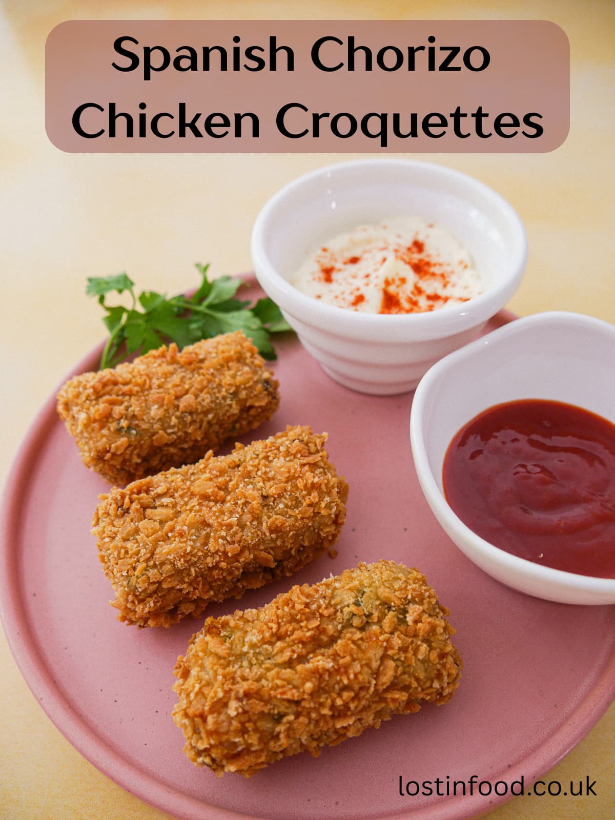 Pinnable image with recipe title and a plate with 3 Spanish chorizo chicken croquettes and bowls of mayonnaise and chilli sauce set alongside.