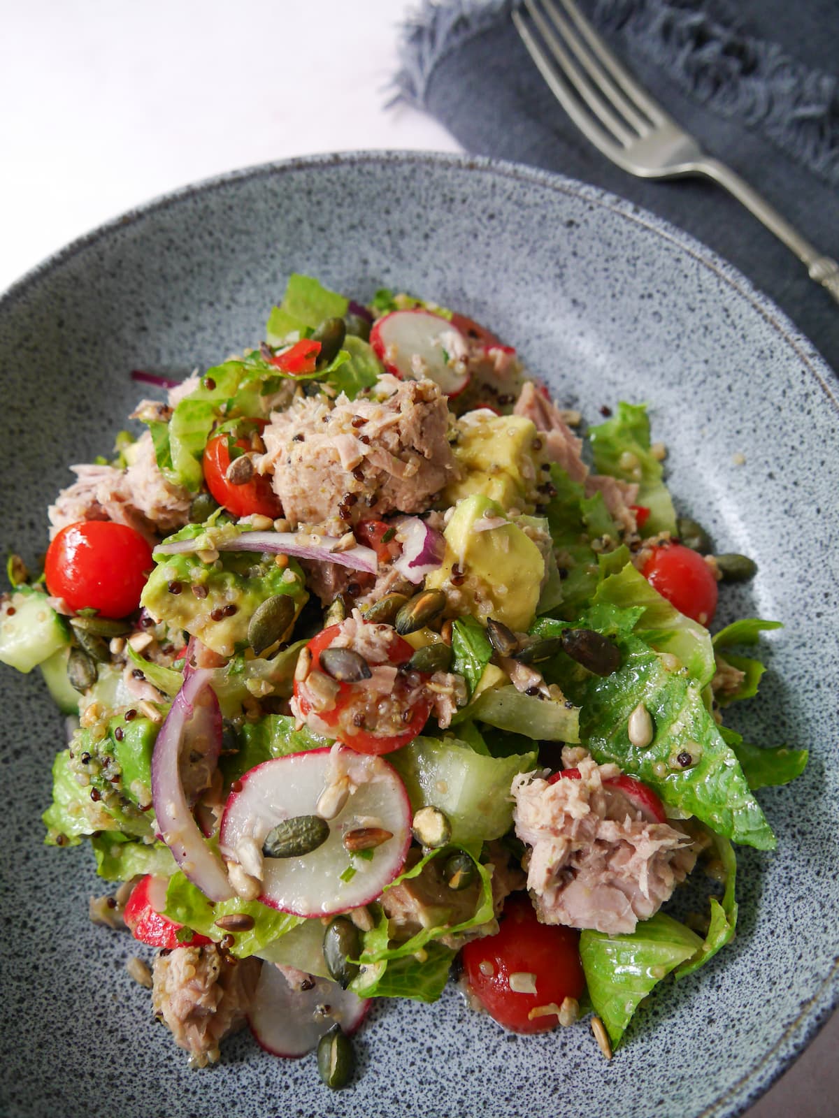 A bowl of tuna, avocado and quinoa salad, with crunchy salad vegetables and garnished with toasted seeds.