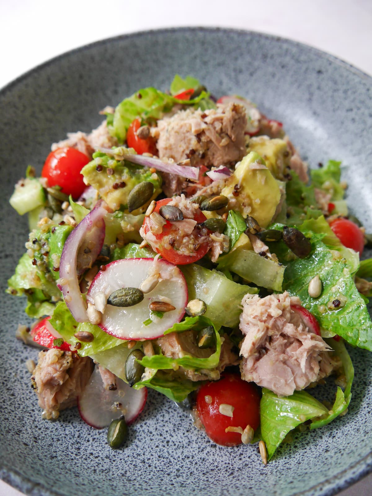 A bowl of tuna, avocado and quinoa salad, with crunchy salad vegetables and garnished with toasted seeds.