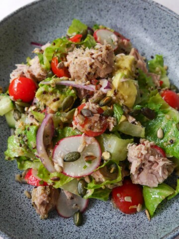A bowl of tuna, avocado and quinoa salad, with crunchy salad vegetables and garnished with toasted seeds.