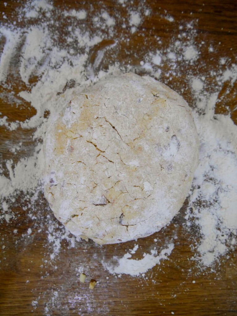 A ball of baked cheese bacon tomato scone dough set on a floured board.