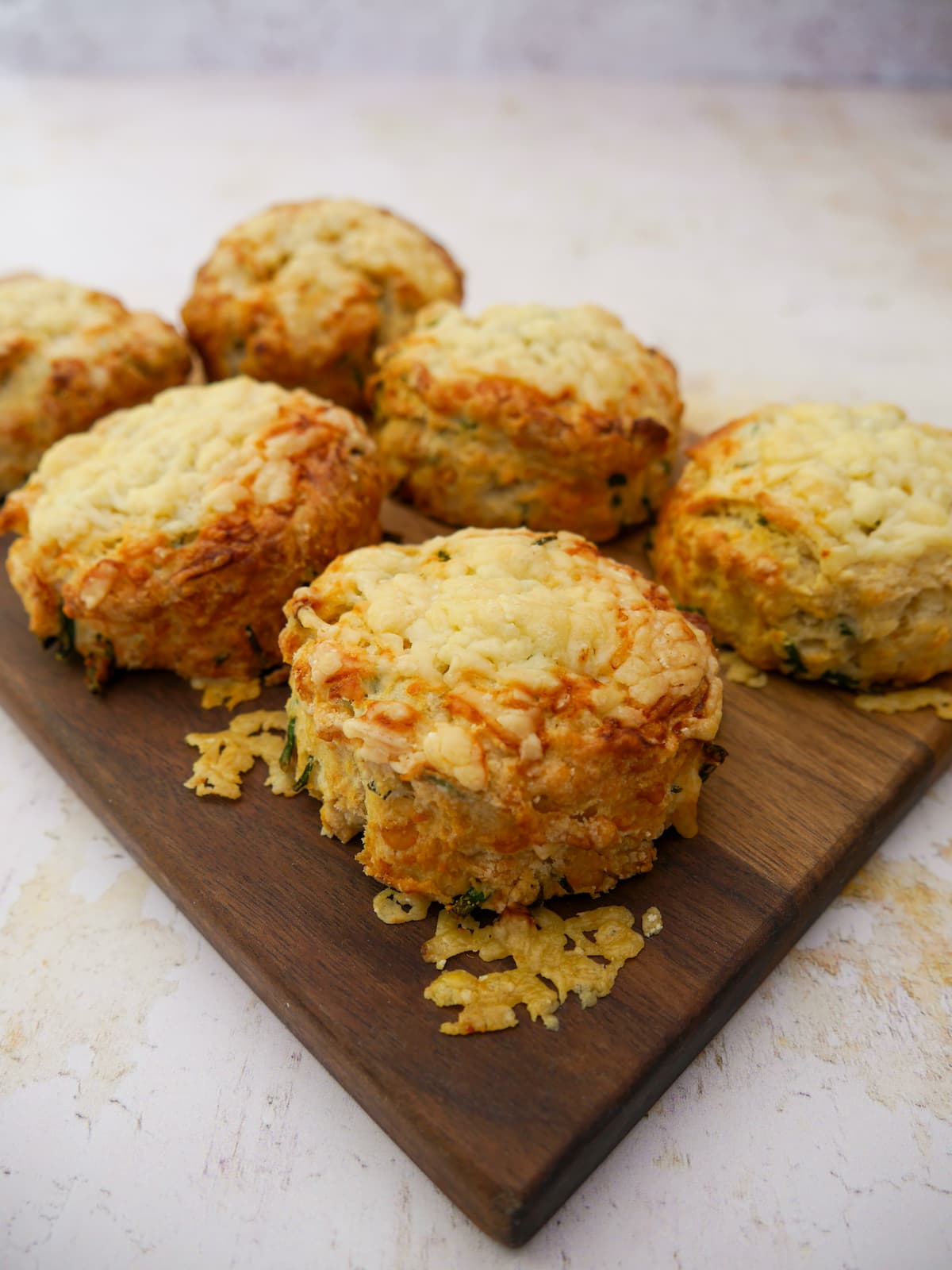 A wooden board topped with 6 cheese and chive scones.