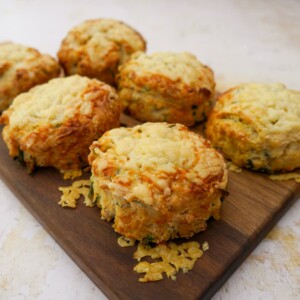 A wooden board topped with 6 cheese and chive scones.