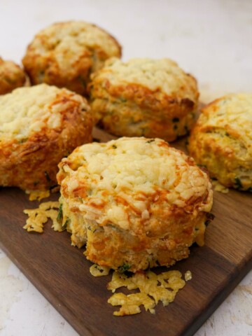 A wooden board topped with 6 cheese and chive scones.