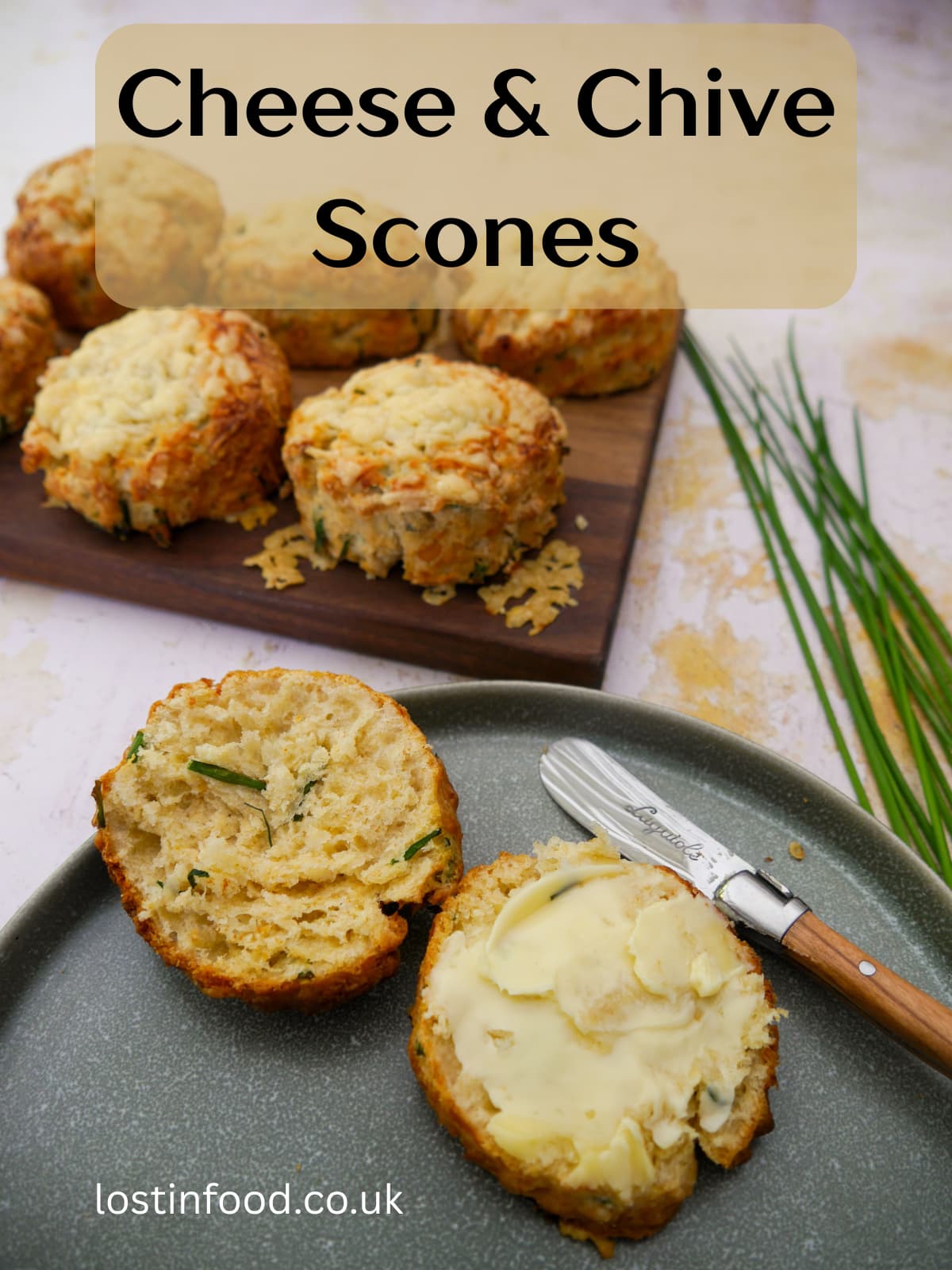 Pinnable image with recipe title and a plate with a halved cheese and chive scone topped with butter. A board of scones is set alongside.
