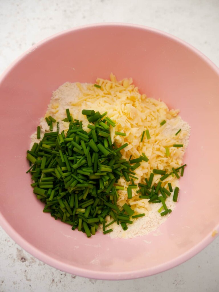 A bowl of rubbed flour, butter and salt with added grated cheddar cheese and finely chopped chives.