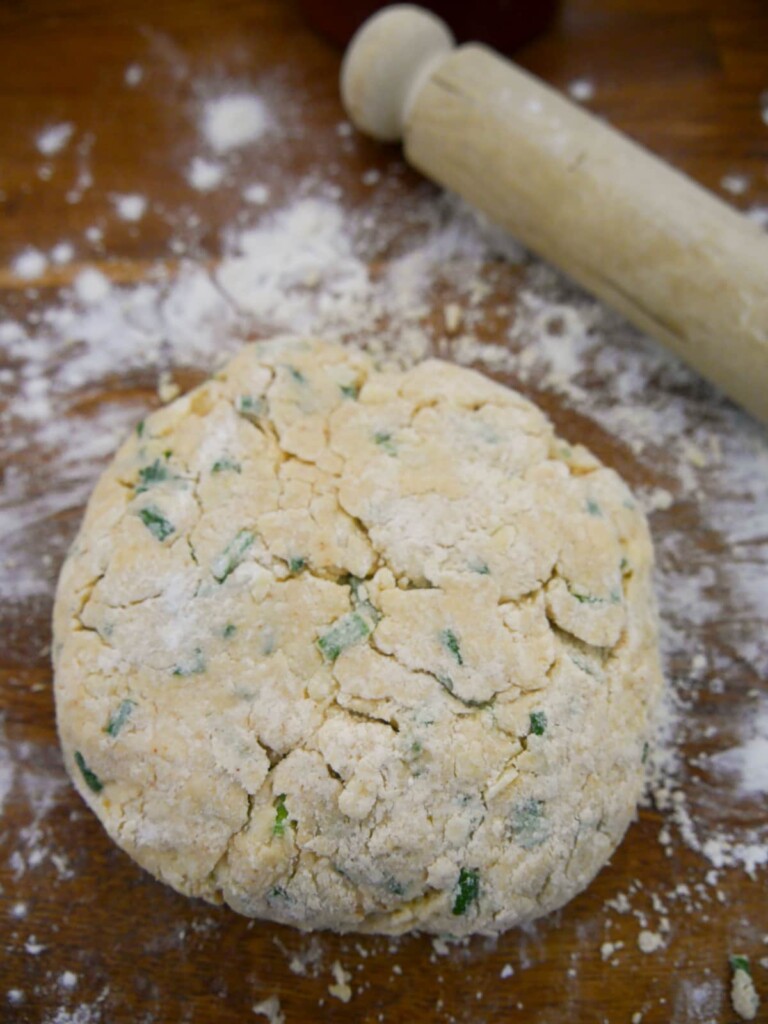 A bowl of cheese and chive scone dough set on a floured board.