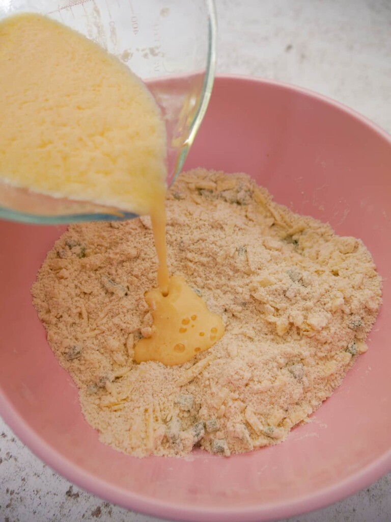 A bowl of dry scone ingredients with beaten egg and buttermilk mixture being added.