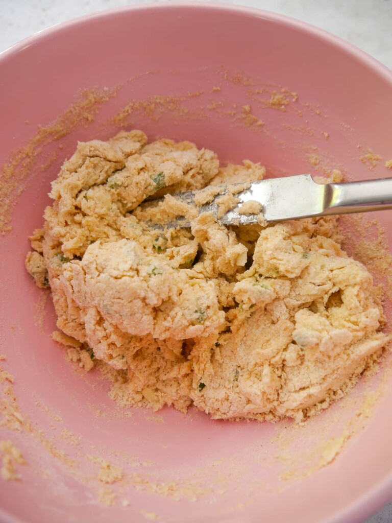 A bowl of cheese and jalapeno scone dough being brought together with a flat kitchen knife.