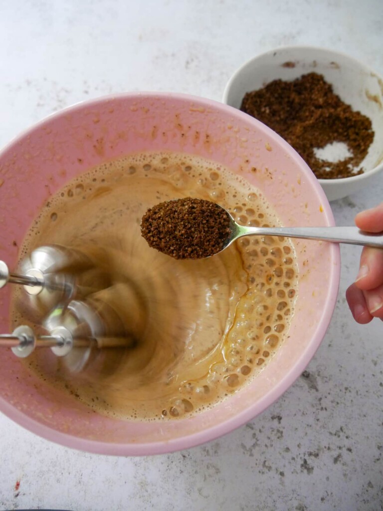 A bowl of whisked sugar and eggs with a mixture of walnut meal, cocoa powder and coffee being added.