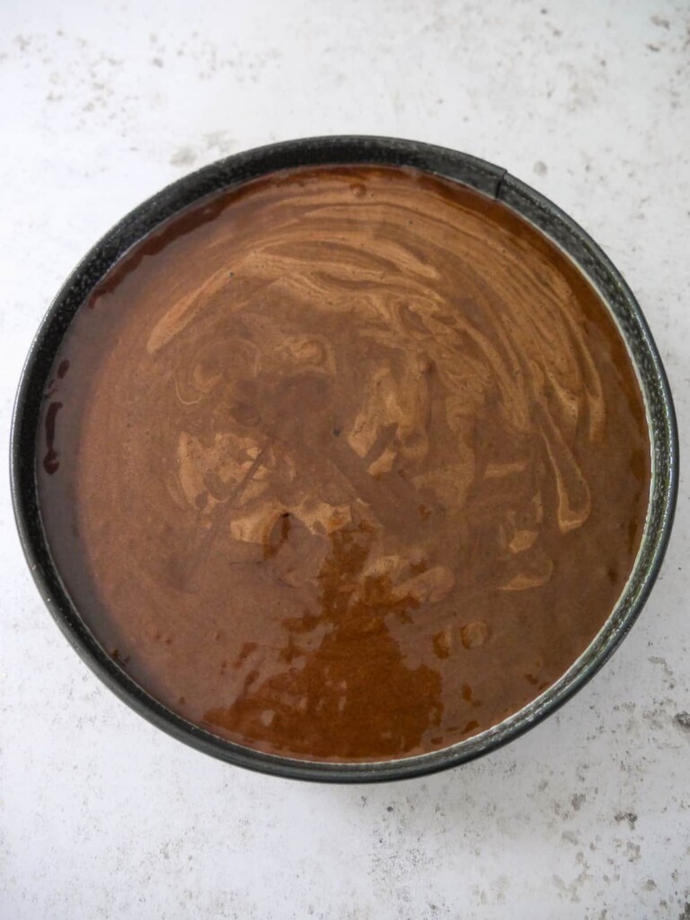A round cake tin with filled with flourless chocolate cake batter.