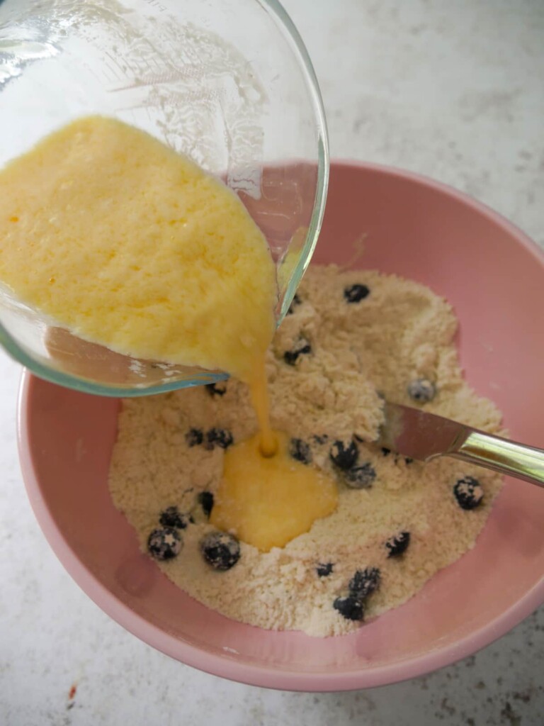 Dry ingredients for lemon and blueberry scones with a mixture of beaten egg and buttercream being added.