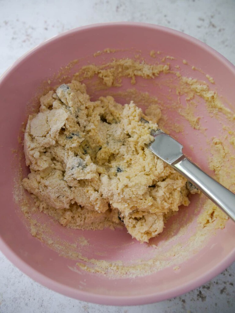 A bowl of lemon and blueberry scone dough being brought together with a flat kitchen knife.