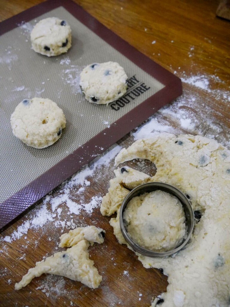 Scone dough being cut with cookie cutter and a lined baking sheet of cut scones set alongside.