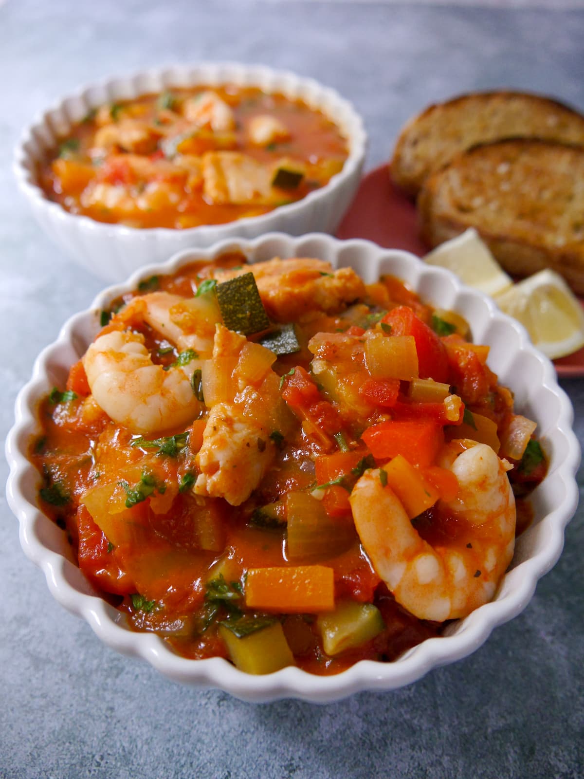 2 bowls of Mediterranean fish soup served with slices of toasted sourdough and wedges of lemon.