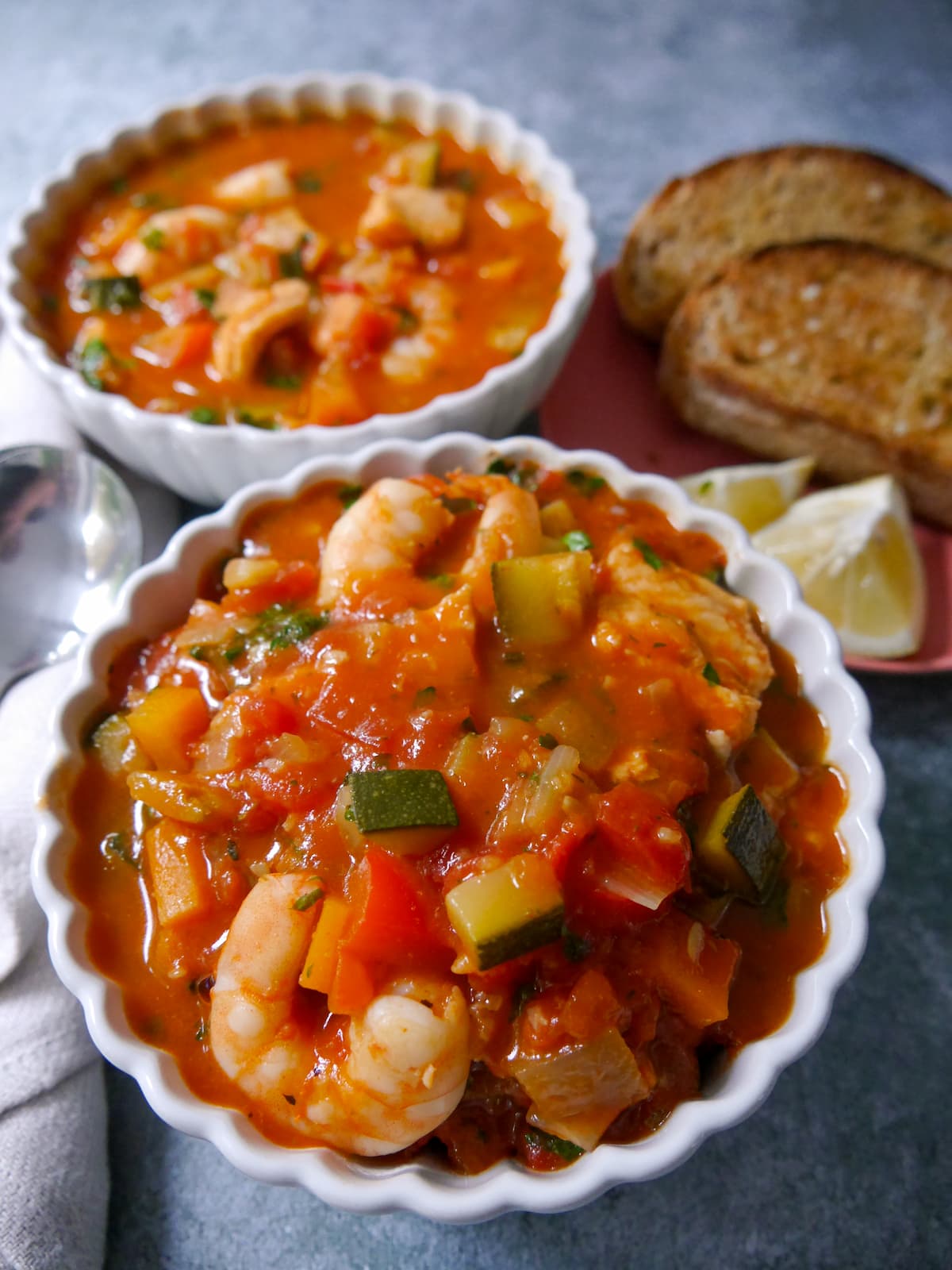 2 bowls of Mediterranean fish soup served with slices of toasted sourdough and wedges of lemon.