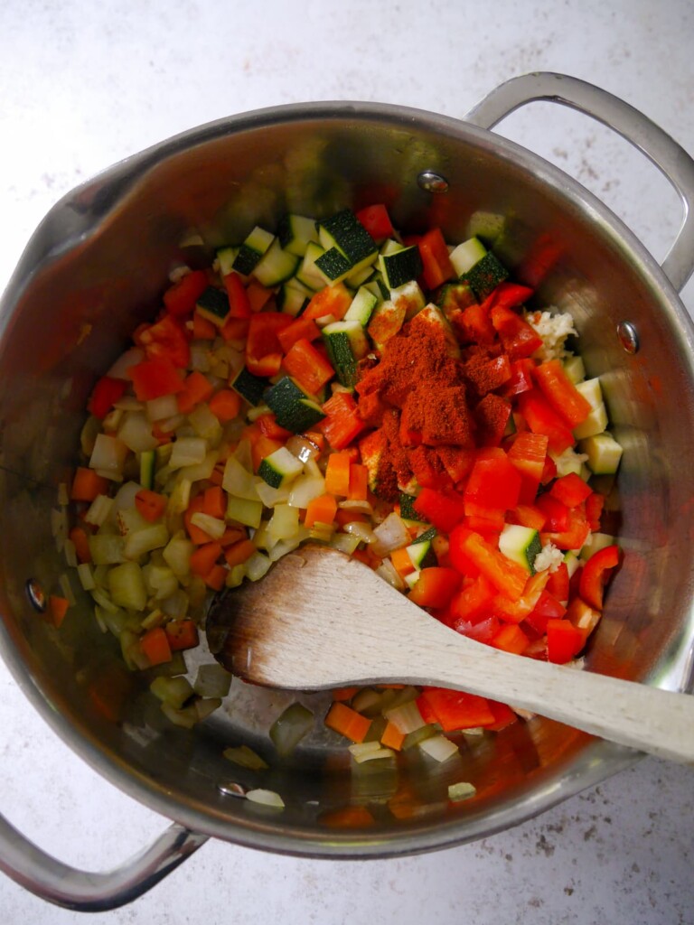 A large soup pan of sauteed vegetables with added dried spices.