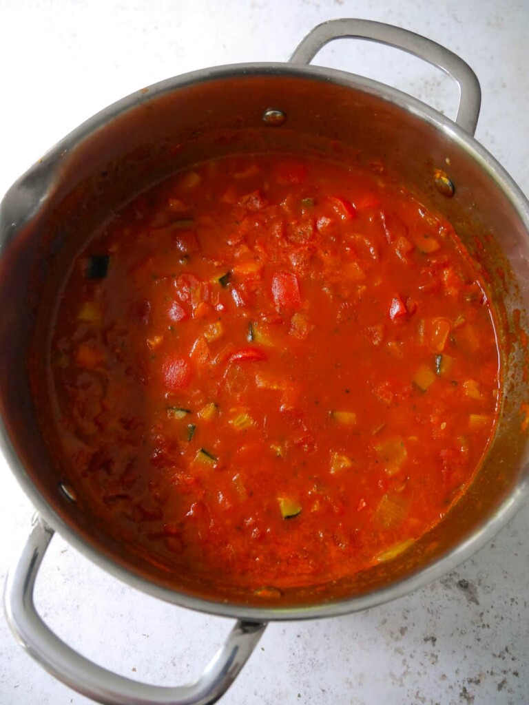 A large soup pan filled with a tomato and cooked vegetable base soup.