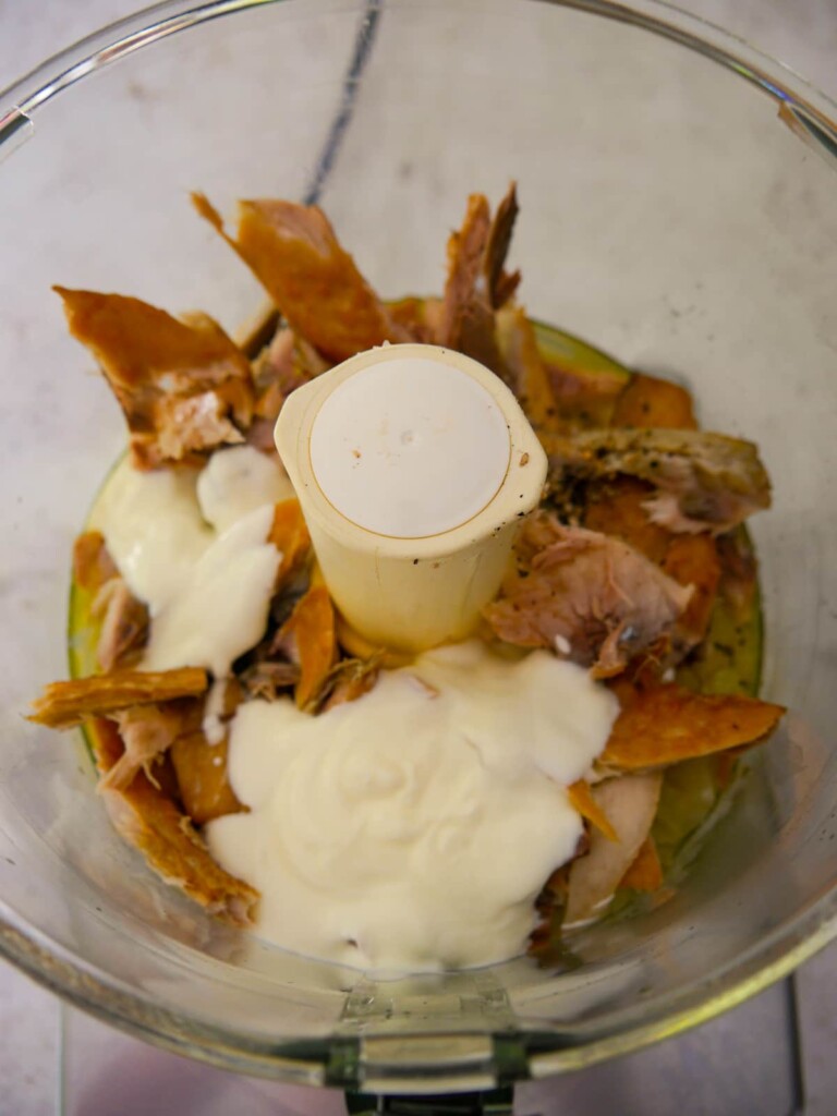 Bowl of a food processor filled with cooked onions, melted butter Greek yogurt and broken up smoked mackerel fillets.