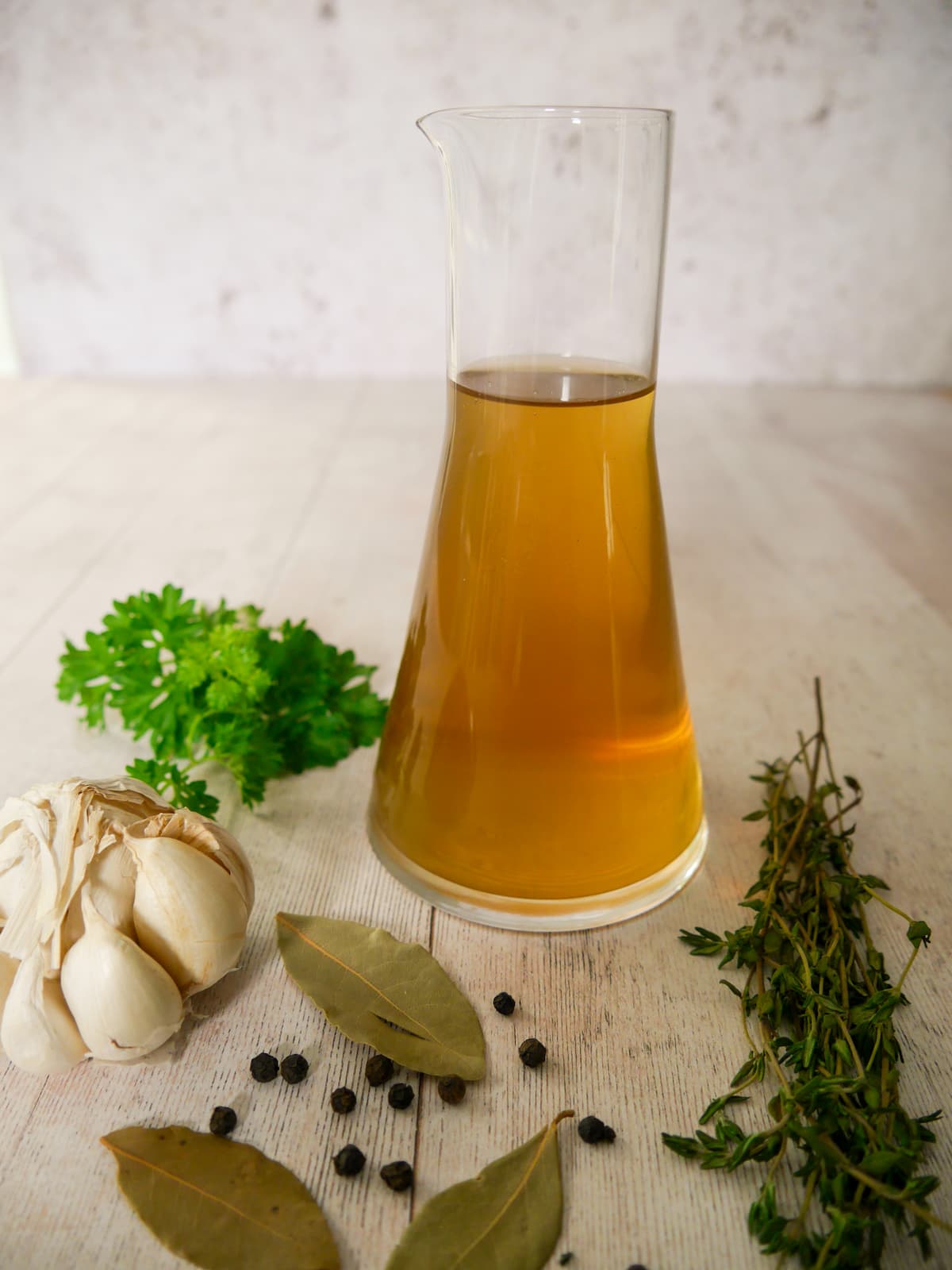 A jug of homemade vegetable stock, with fresh herbs and aromatics set alongside.