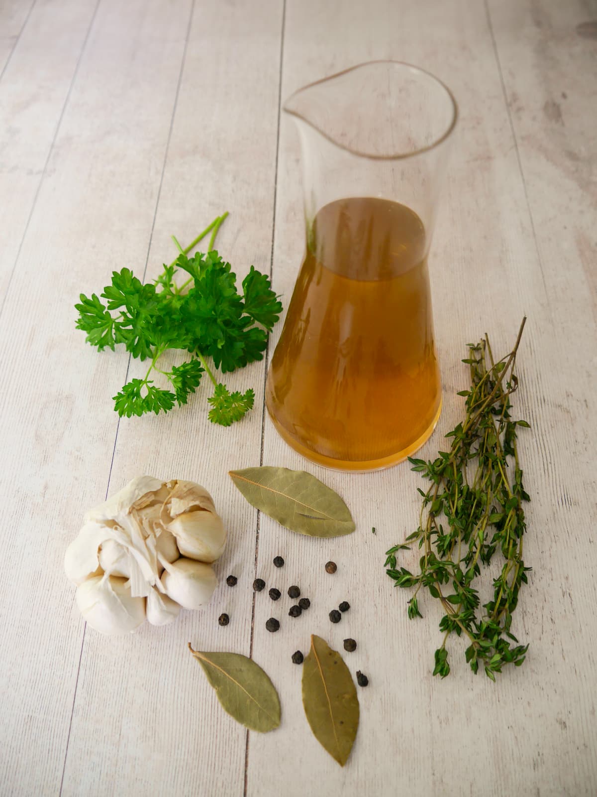 A jug of homemade vegetable stock, with fresh herbs and aromatics set alongside.