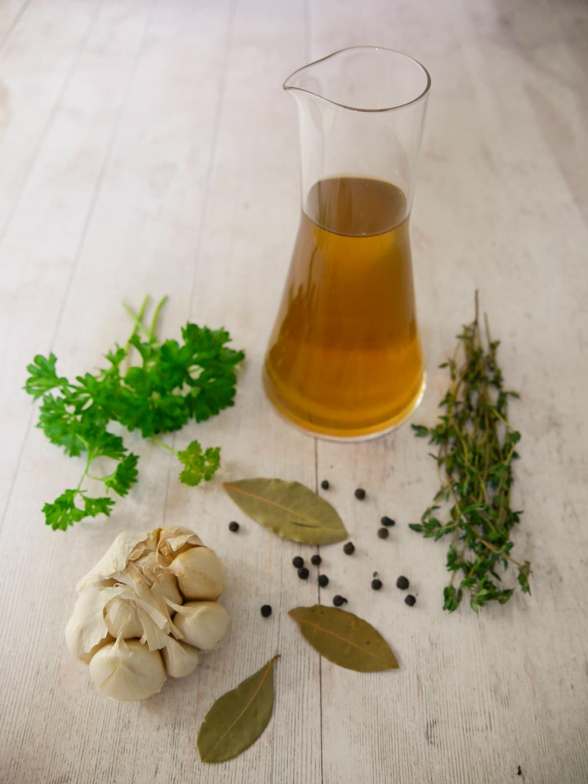 A jug of homemade vegetable stock, with fresh herbs and aromatics set alongside.