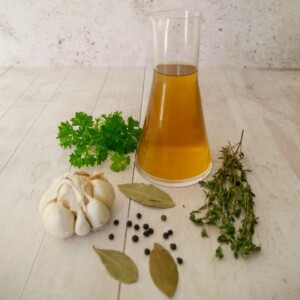 A jug of homemade vegetable stock, with fresh herbs and aromatics set alongside.