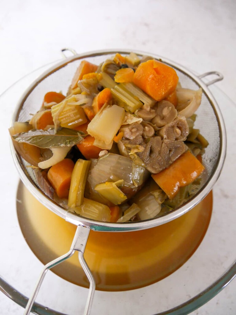 A wire sieve filled with cooked vegetables, set over a large bowl to allow the vegetable stock to drain off.